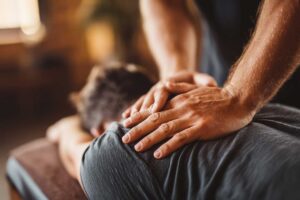 A person sitting at a desk, gently stretching their neck while touching their jaw with one hand.
